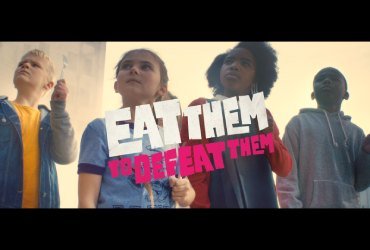 A promotional still from ITV and Veg Power's campaign is shown where young children are armed with kitchen utensils with determined looks on their faces. Text over the image says Eat Them to Defeat Them.