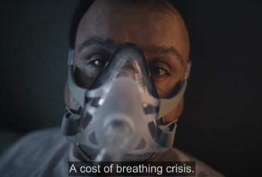 A man is wearing a mask to help him breathe. "A cost of breathing crisis" is written on top of the image.