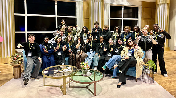 A diverse group of 24 young people sit close together on the sofa of This Morning, in the studio. They are smiling and posing to camera and some have playful expressions on their faces.
